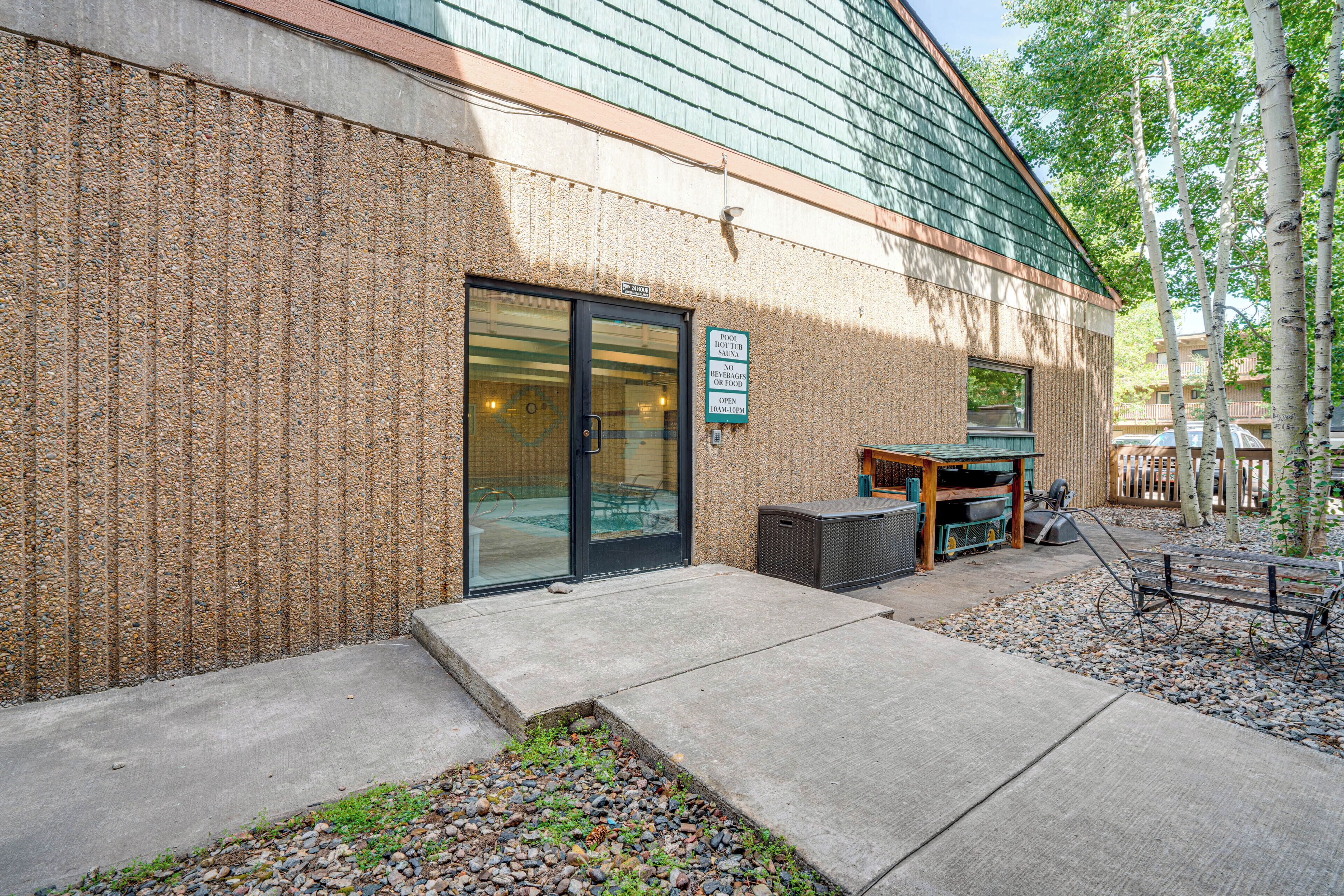A building with a pebble-textured exterior, a glass door entrance, and a sign indicating a 24-hour pool hot tub and sauna.