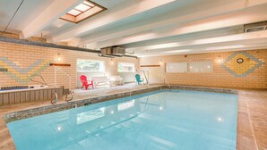 Una piscina interior con pared de azulejos, una silla roja y una silla azul.
