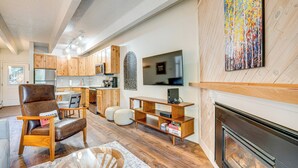 Una sala de estar moderna con chimenea, piso de madera, un sillón de cuero y un televisor montado en la pared.