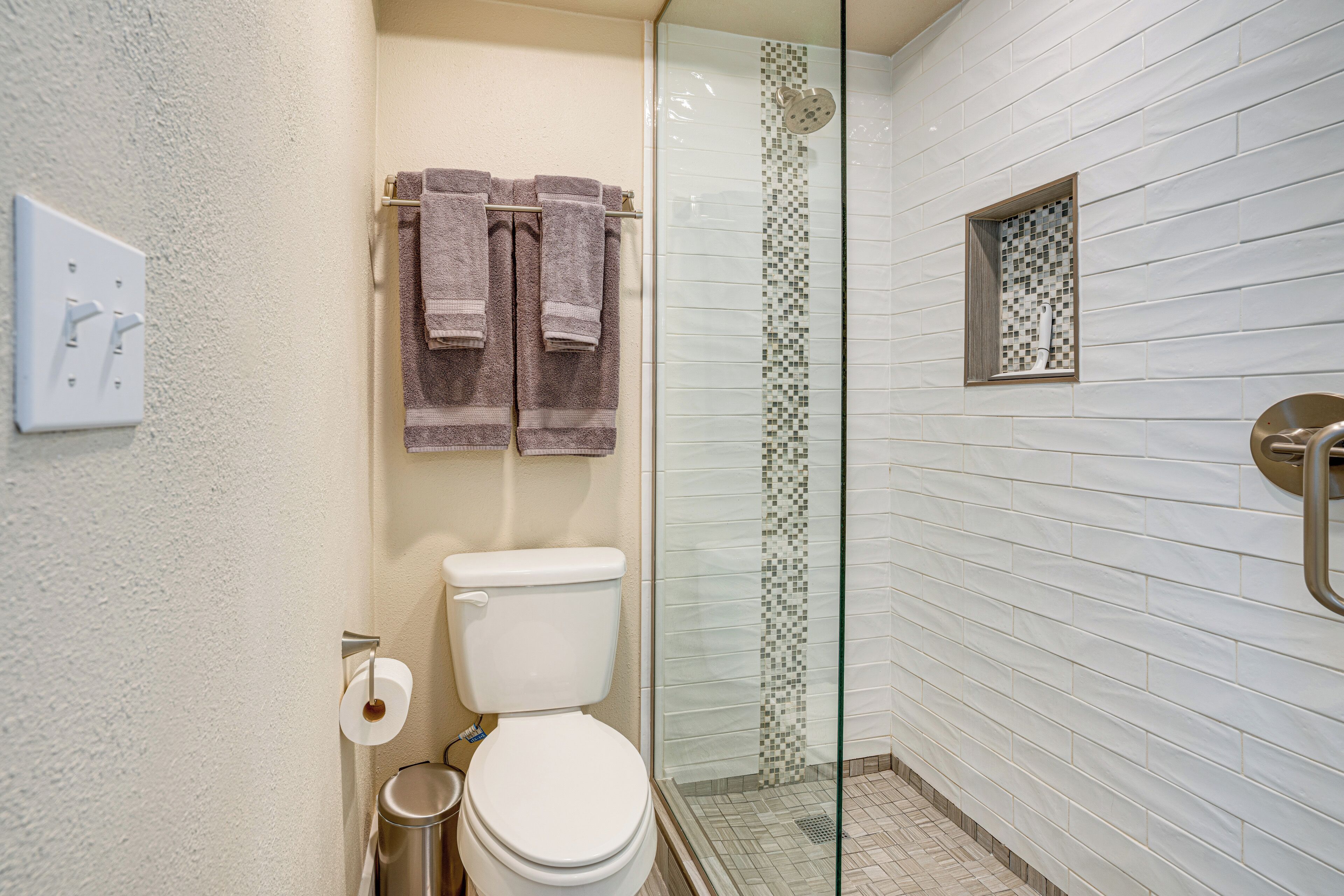 A bathroom with a toilet, a glass shower enclosure, and a towel rack with towels.