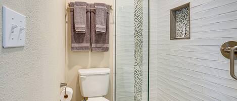 A bathroom with a toilet, a glass shower enclosure, and a towel rack with towels.