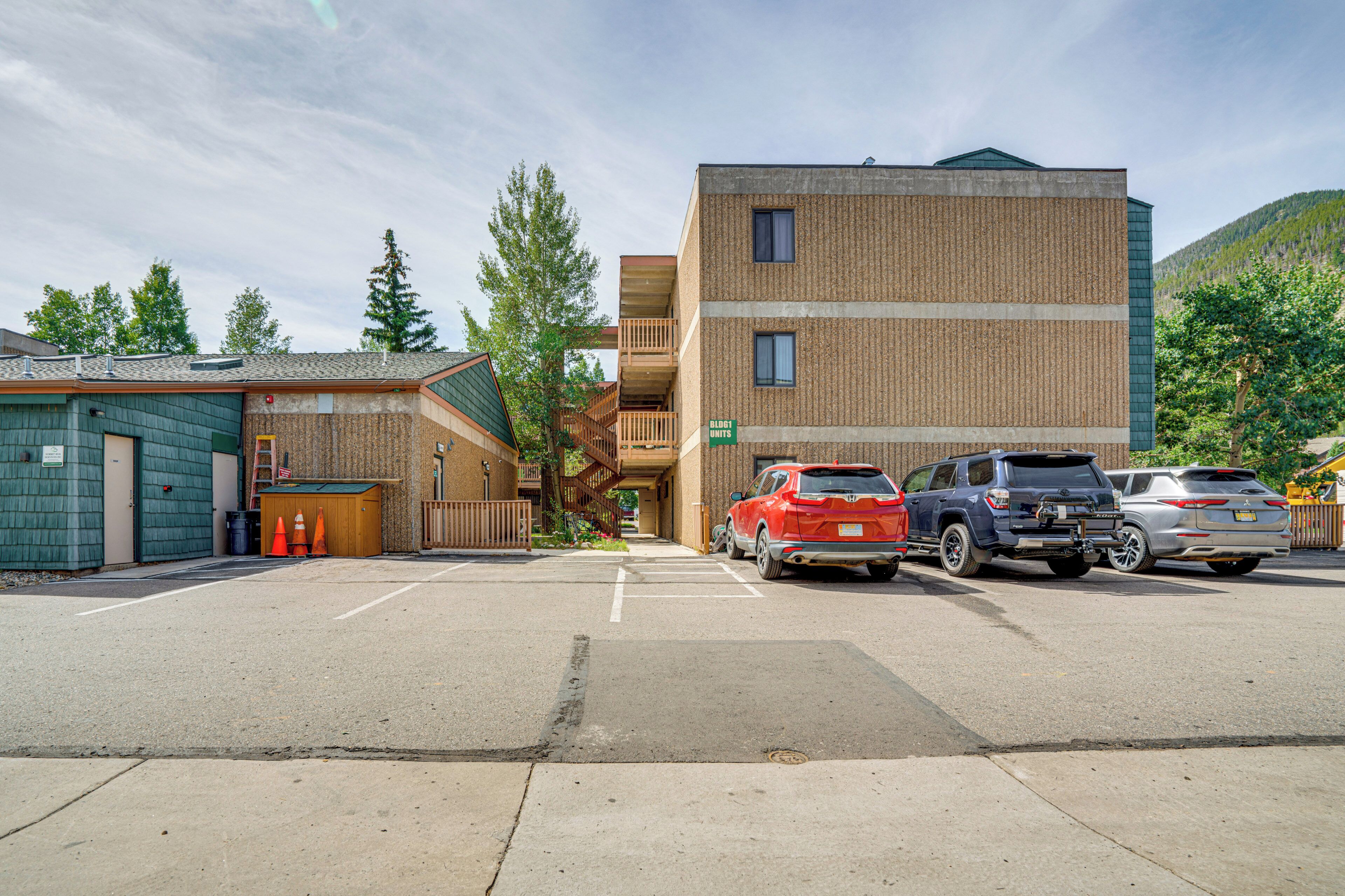 A parking lot with several cars, a multi-story building with a brick facade, and a mountain in the background.