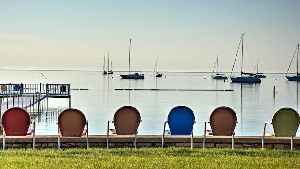 A waterfront view with a row of chairs facing the water, a dock, and several boats. - Cozy Cottage Duplex: Walk to Peninsula State Park! (Ephraim)