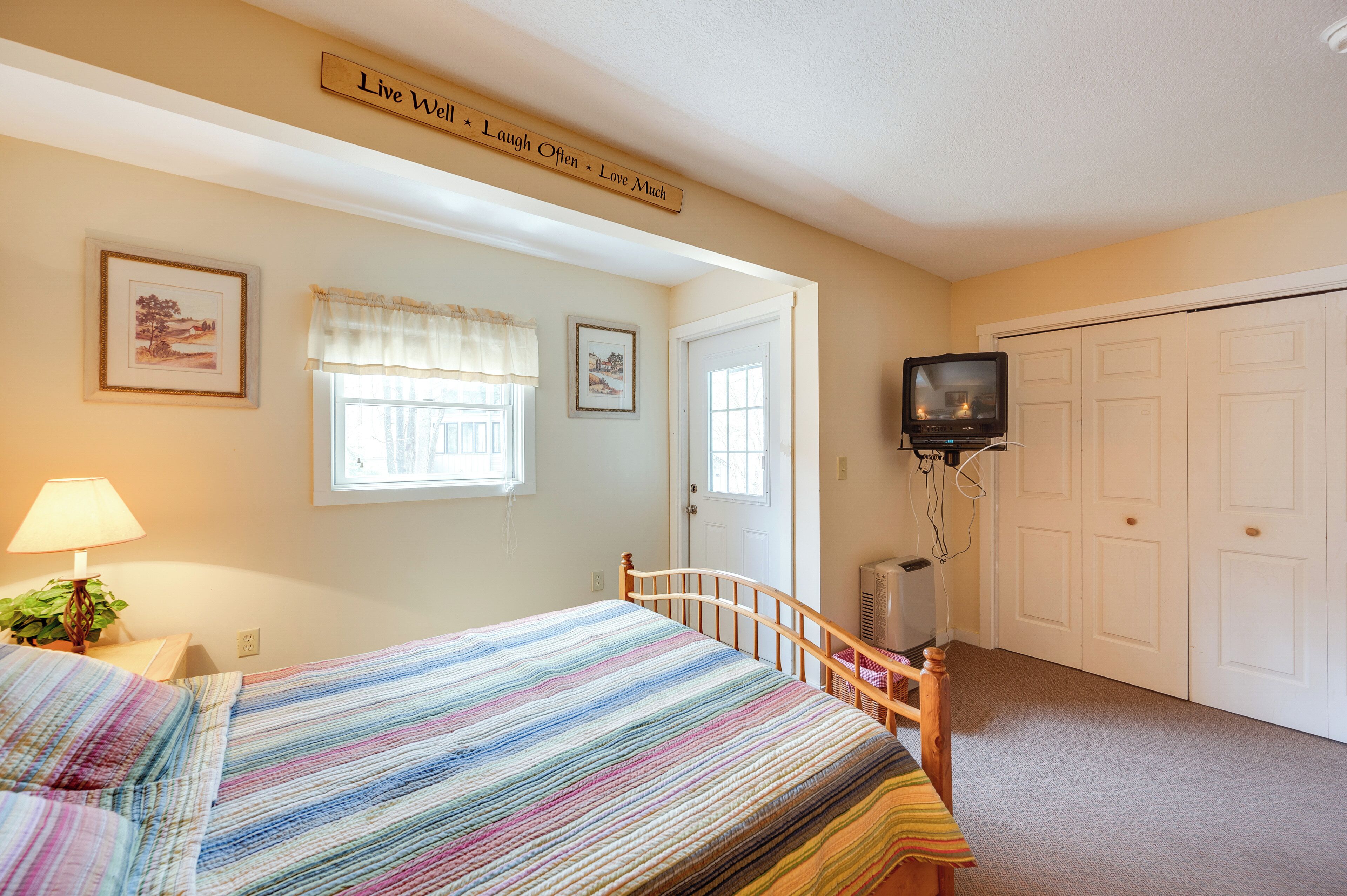 A bedroom with a bed, a television, a door, and a wall-mounted sign.