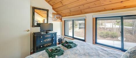 A bedroom with a large bed, a dresser, a mirror, and a window with a view of trees.