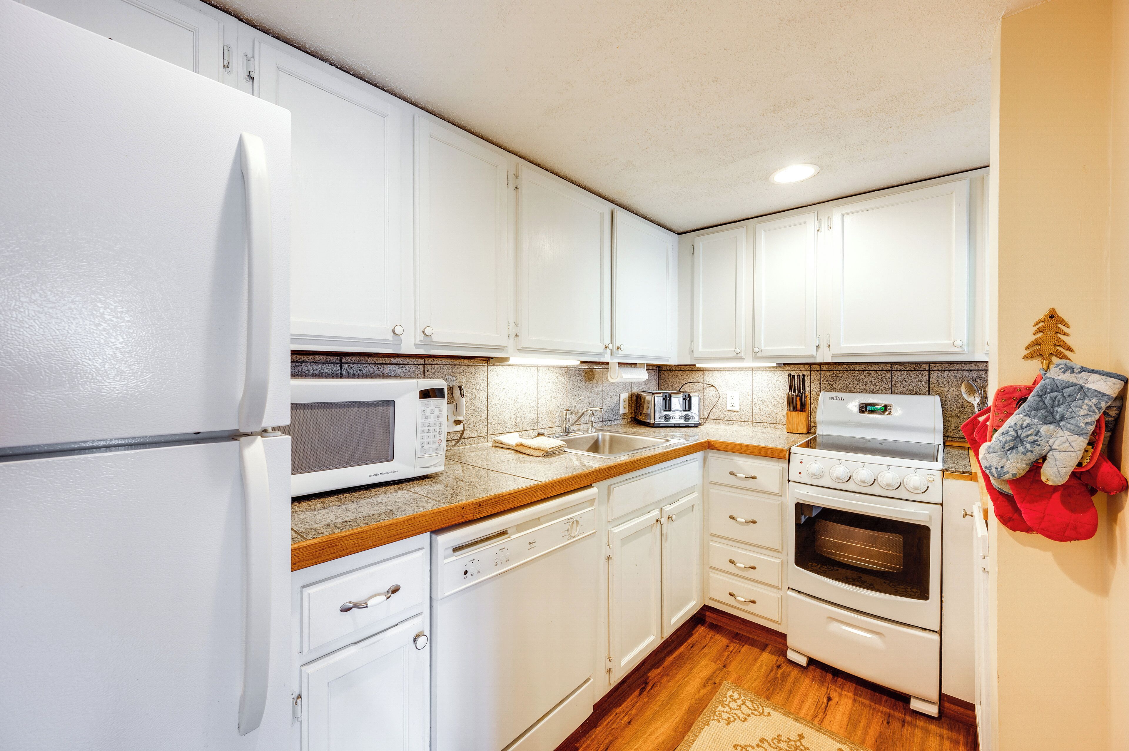 A kitchen with white cabinets, a microwave, a toaster, a sink, a dishwasher, and an oven.
