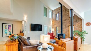 A modern living room with a brick wall, leather sofas, a flat-screen TV, and a wooden coffee table. - < 1 Mi to Dtwn: Creekside Frisco Home w/ Fire Pit (Frisco)