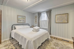 A neatly made bed with a white quilt, a framed map on the wall, and a window with curtains. - Charming Sutton Cottage: Walk to Lake & Farm! (Sutton)