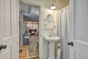 A bathroom with a white sink, a mirror, and a shower curtain. - Charming Sutton Cottage: Walk to Lake & Farm! (Sutton)