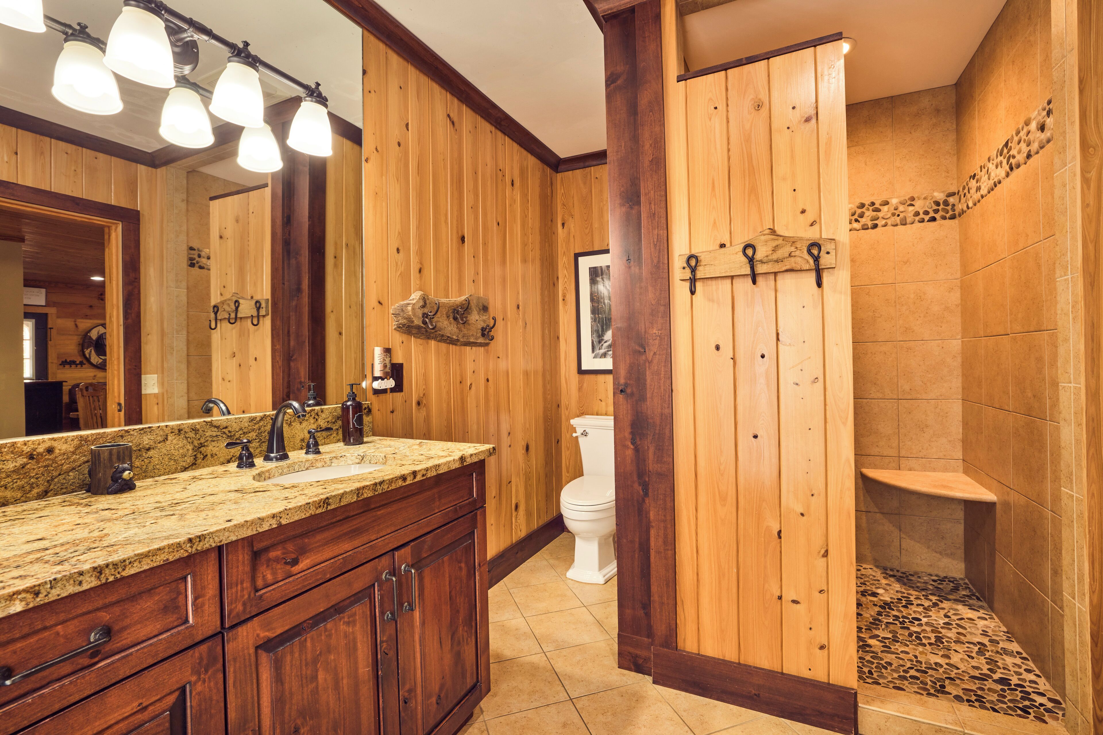A wooden bathroom with a granite countertop, a white toilet, and a shower area.