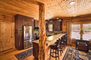 A wooden interior with a central island, bar stools, and a large window. - 25-acre Mountain Retreat w/ Trails, Pond, Hot Tub (Penrose)