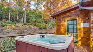 Una cabaña de madera con jacuzzi en una terraza, rodeada de follaje otoñal.