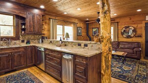 Interior de una cabaña de madera con cocina que cuenta con gabinetes de madera oscura, encimera de granito y lavavajillas integrado.