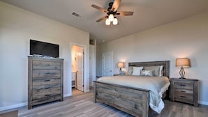 A bedroom with a wooden bed, two bedside tables with lamps, a ceiling fan, and a TV on a wooden dresser. - 'sea Shell Chalet': Oceanfront Surfside Beach Gem (Freeport)