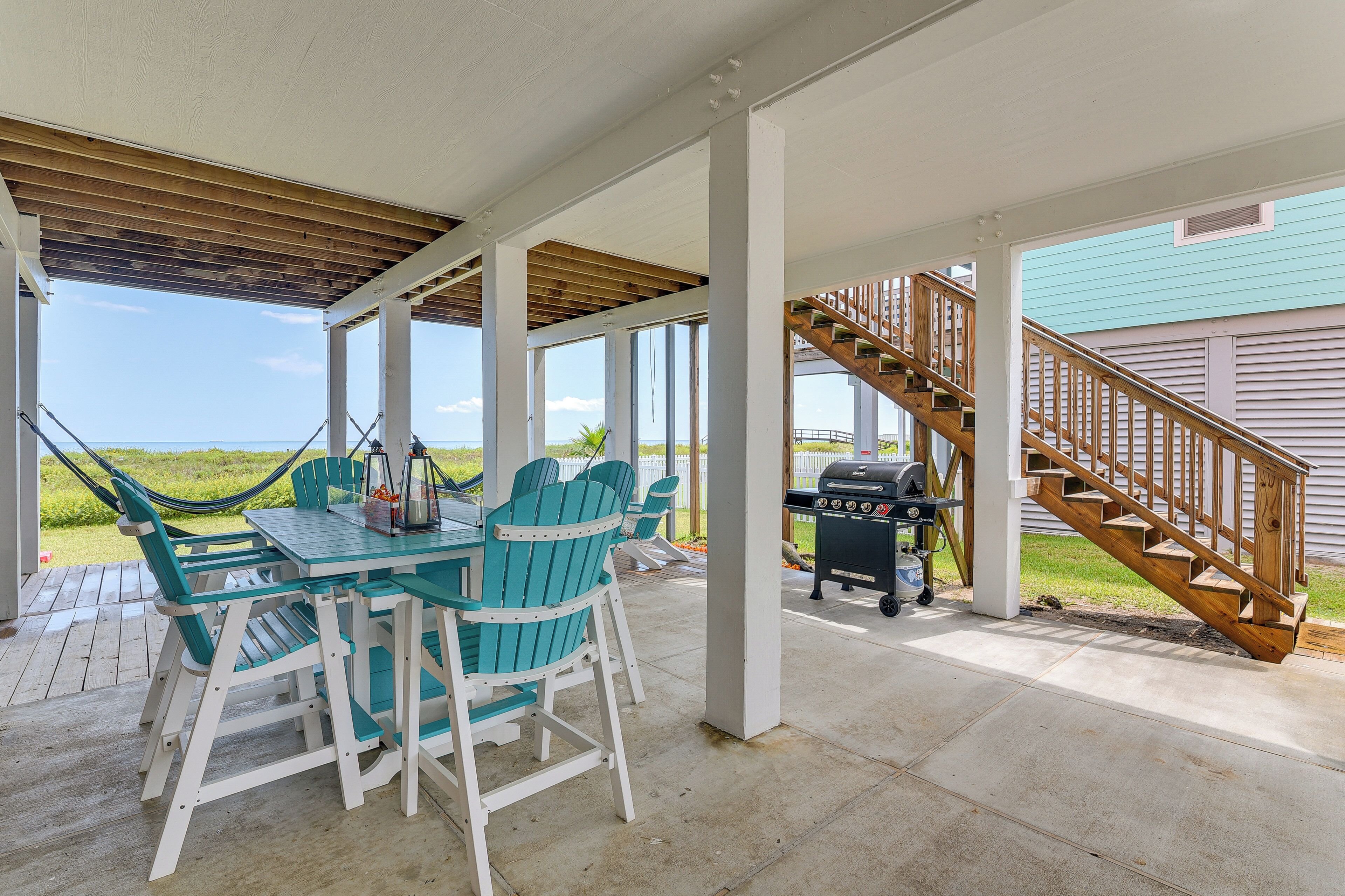 A covered patio with a table and chairs, a grill, and a wooden staircase.