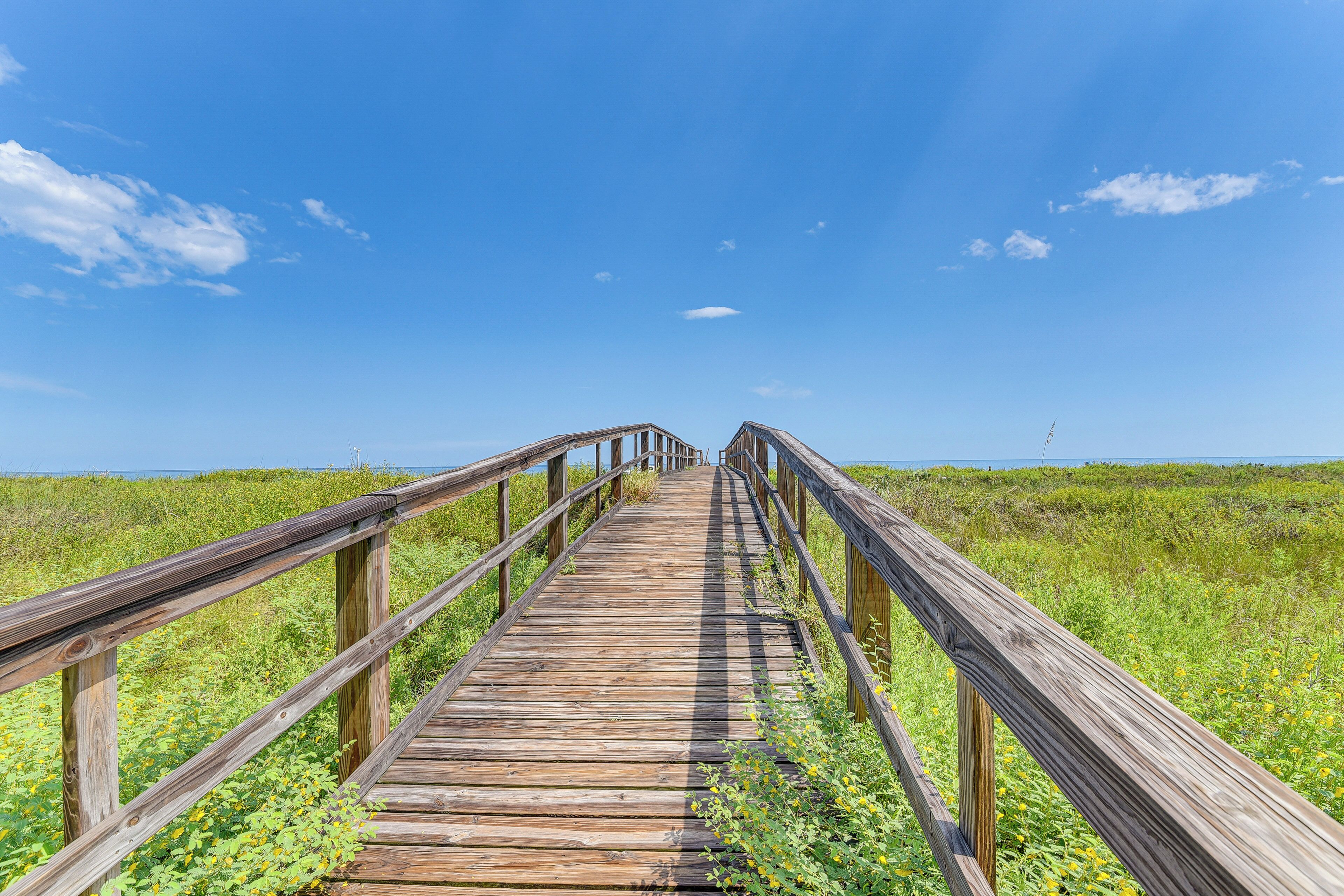 A wooden boardwalk leading to a beach with a clear blue sky.