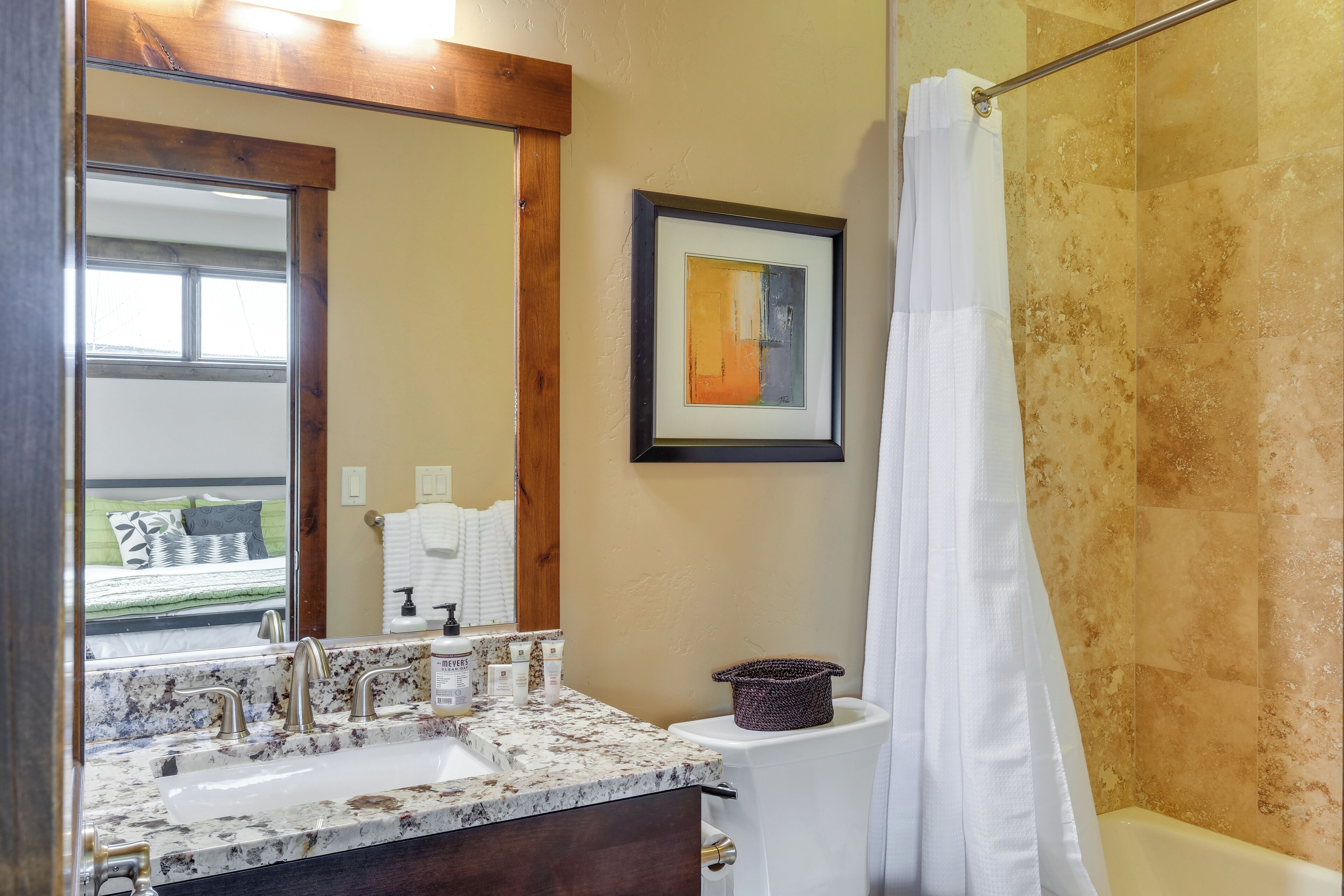A bathroom with a sink, mirror, framed artwork, and a shower curtain.