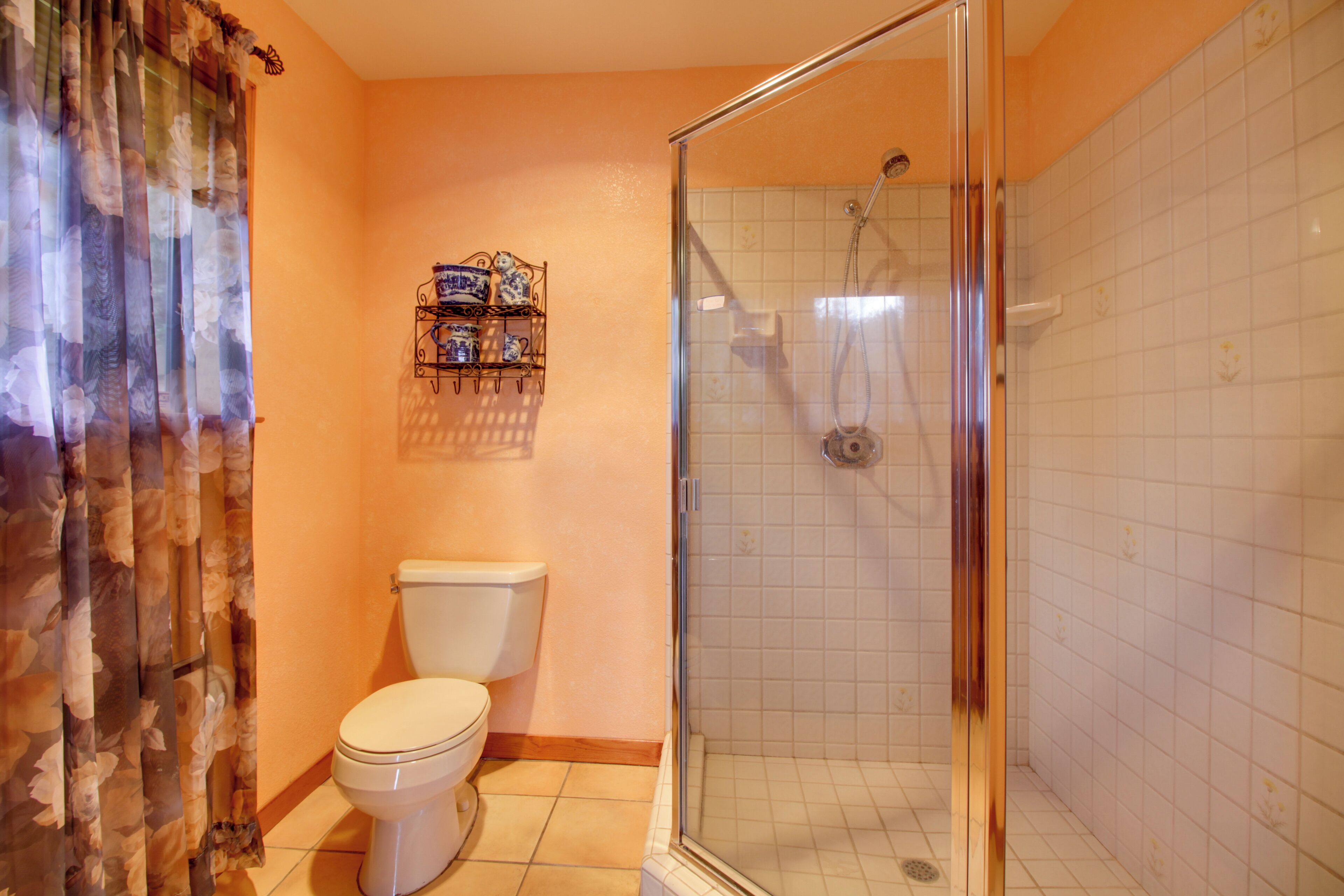 A bathroom with a toilet, a shower with a glass door, and a shelf with toiletries.