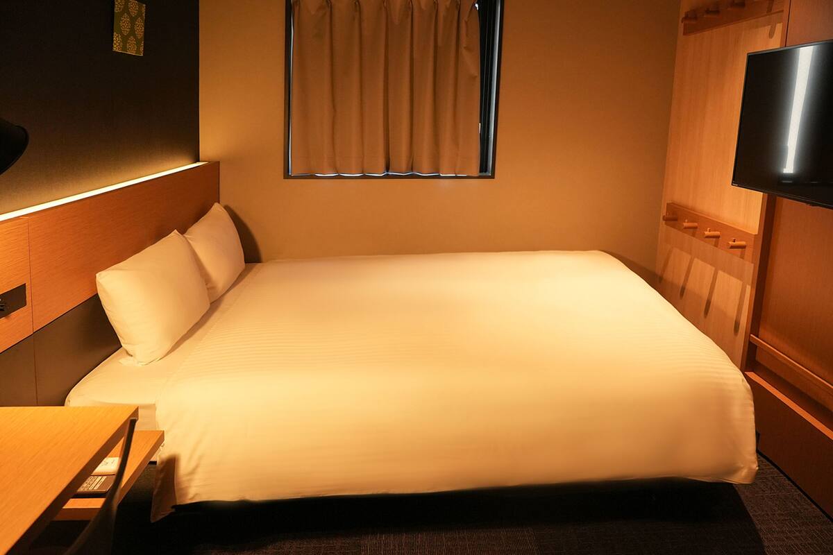 A hotel room with a bed, a TV mounted on the wall, and a window with curtains.