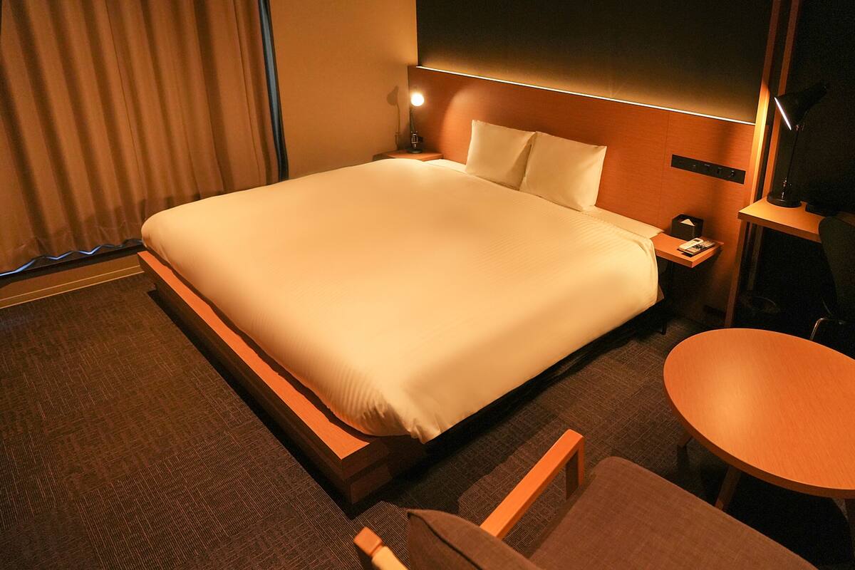 A hotel room with a large bed, a bedside table with a lamp, a small round table, and a chair.