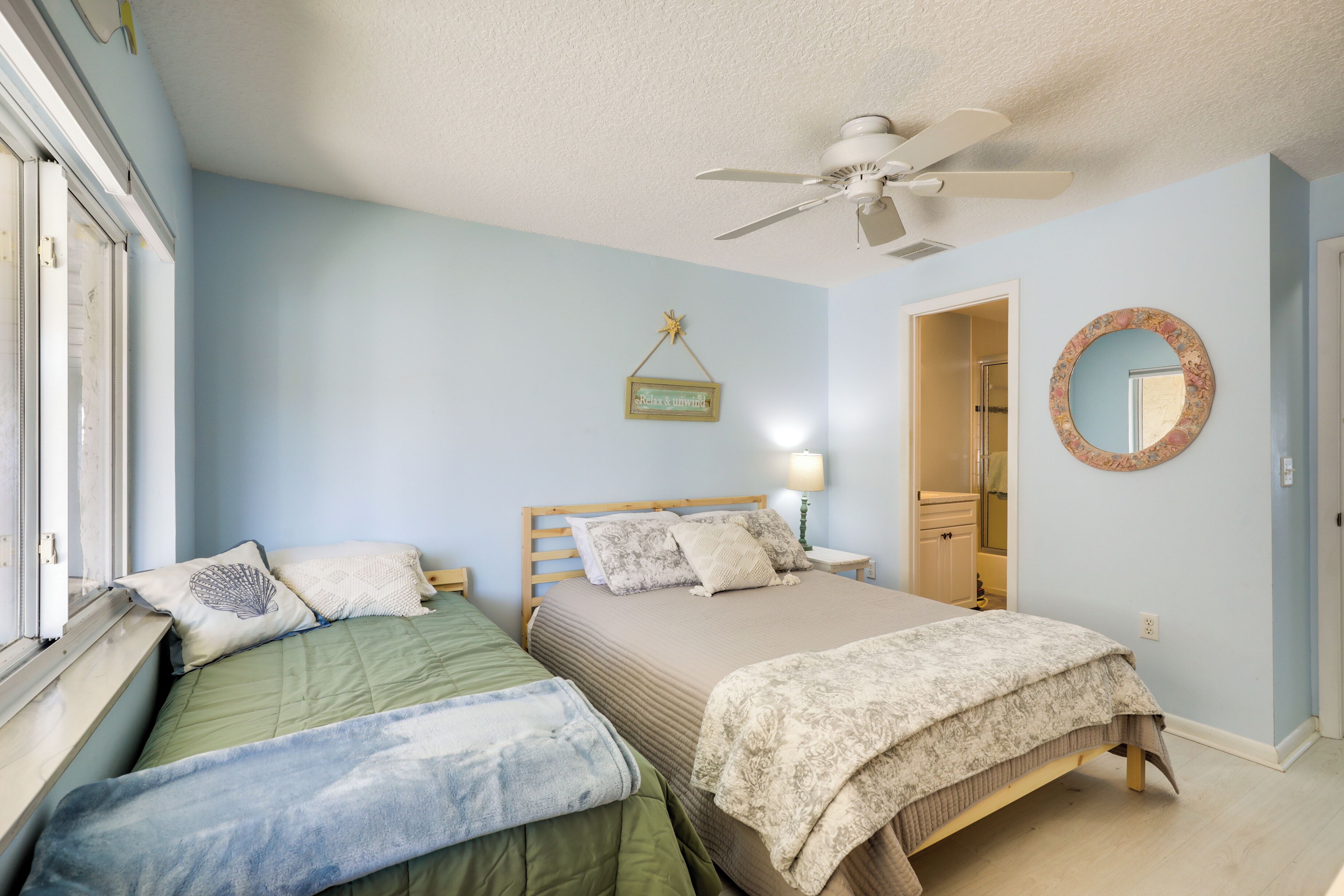 A bedroom with two beds, a ceiling fan, a mirror, and a door leading to another room.