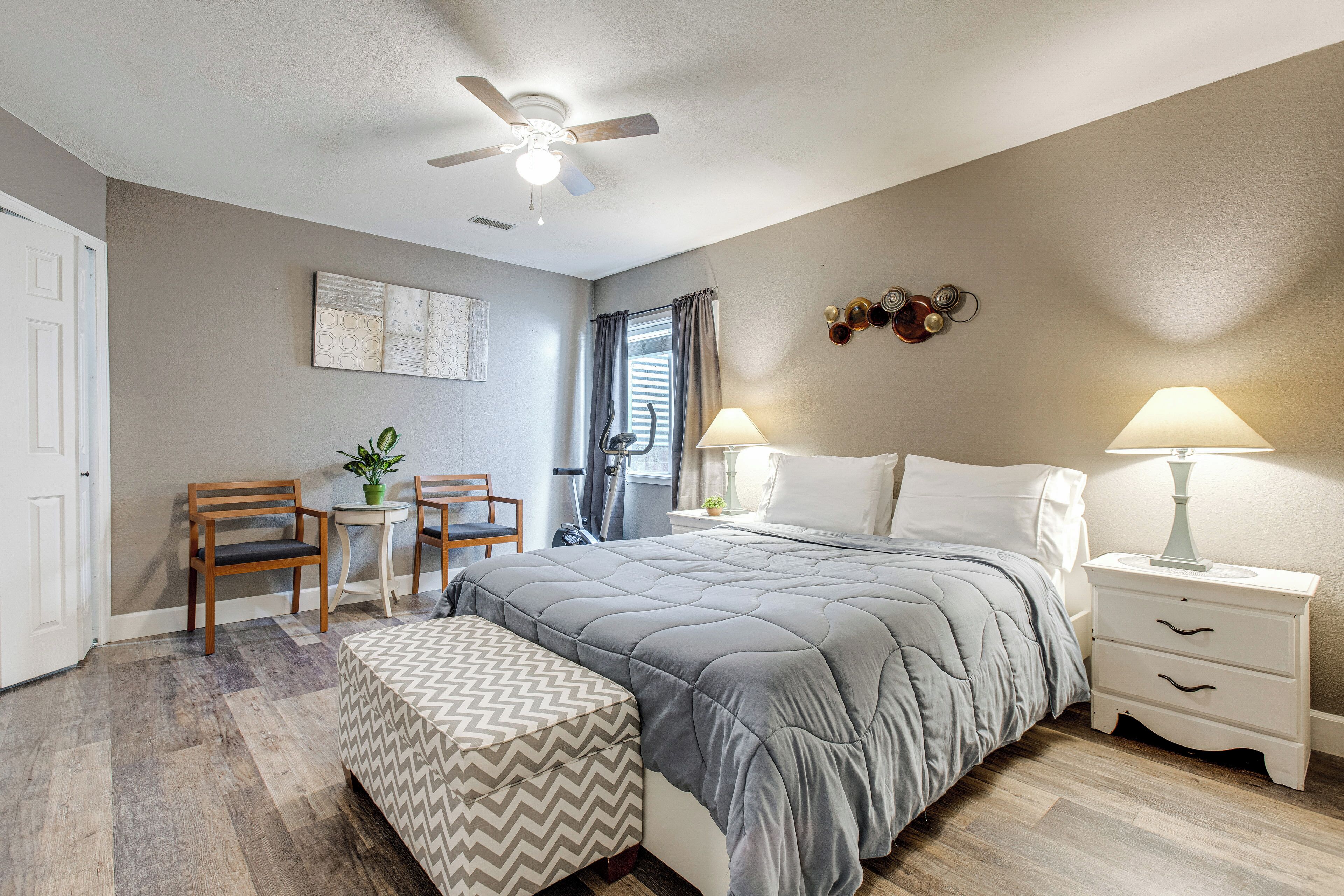A bedroom with a bed, two bedside tables, a chair, a small table, and a ceiling fan.