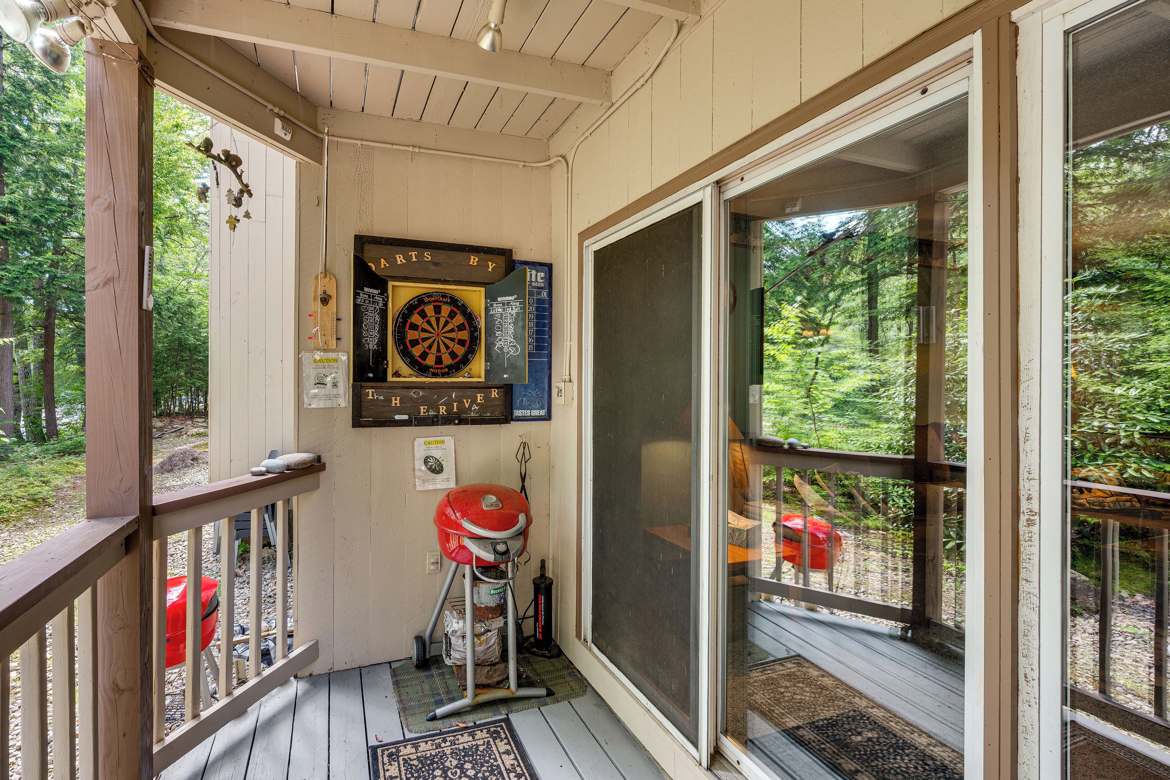 A porch with a dartboard, a grill, and a view of the forest.