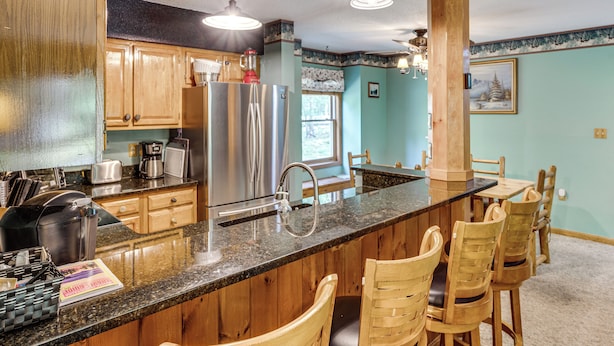 A kitchen with wooden cabinets, stainless steel appliances, a granite countertop, and a bar area with wooden chairs. - Riverfront Retreat w/ Deck: 1 Mi to Loon Mtn! (Lincoln)