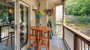 A wooden deck with a round table and four stools, a glass door leading outside, and a view of a pond. - Riverfront Retreat w/ Deck: 1 Mi to Loon Mtn! (Lincoln)