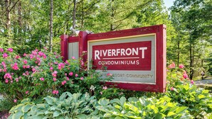 A sign for Riverfront Condominiums in a lush, green setting with flowering plants. - Riverfront Retreat w/ Deck: 1 Mi to Loon Mtn! (Lincoln)