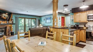 A kitchen with wooden cabinets, a dining table, and a large window. - Riverfront Retreat w/ Deck: 1 Mi to Loon Mtn! (Lincoln)