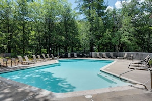 A rectangular pool with a clear blue water surface, surrounded by a concrete deck with lounge chairs and a wooden fence.