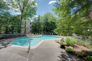 A swimming pool with lounge chairs and a fence, surrounded by trees.
