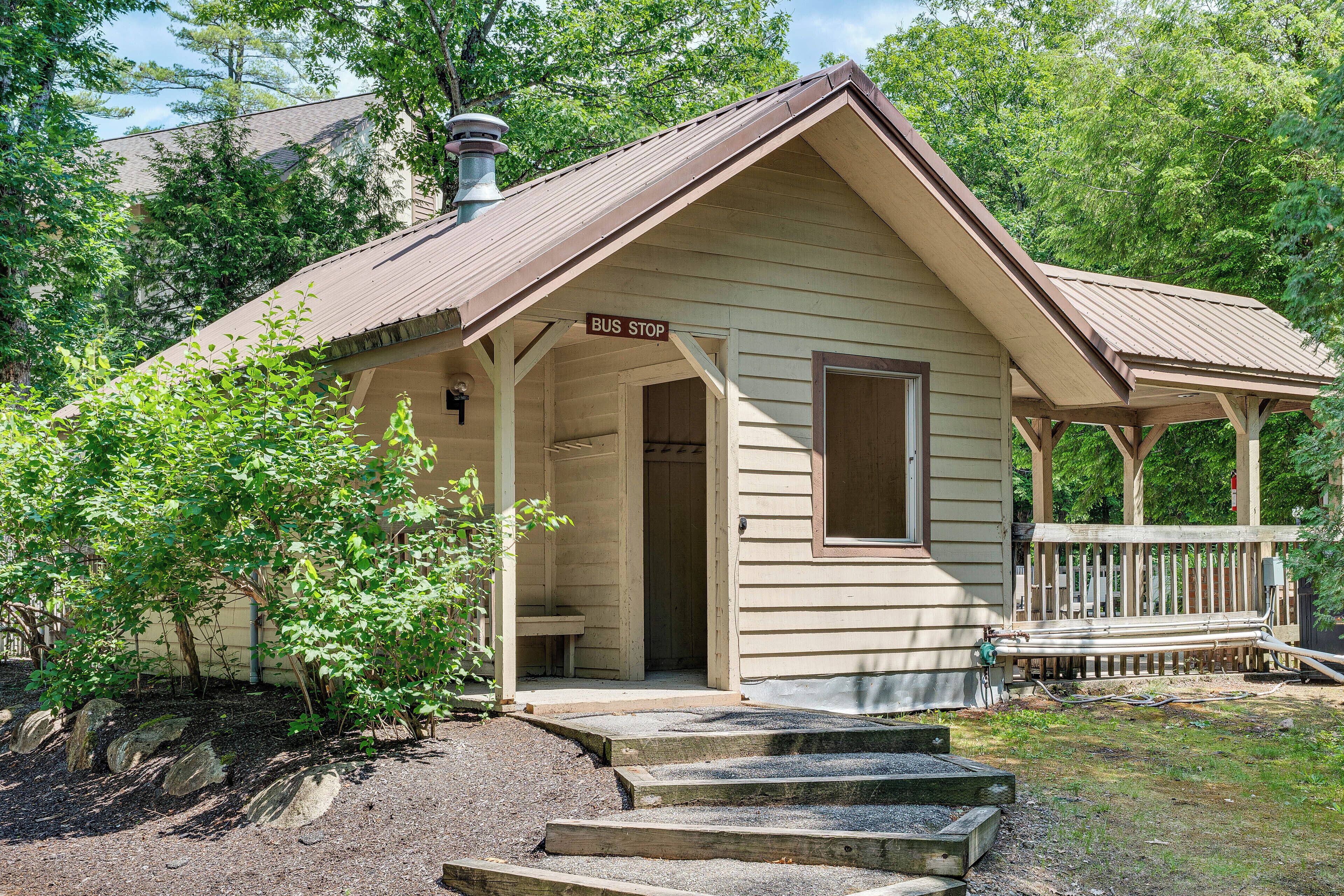 A small, single-story building with a porch, a sign reading 'BUS STOP,' and a wooden fence in the background.