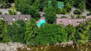 An aerial view of a residential area with houses, a swimming pool, and a tennis court surrounded by dense greenery. - Riverfront Retreat w/ Deck: 1 Mi to Loon Mtn! (Lincoln)