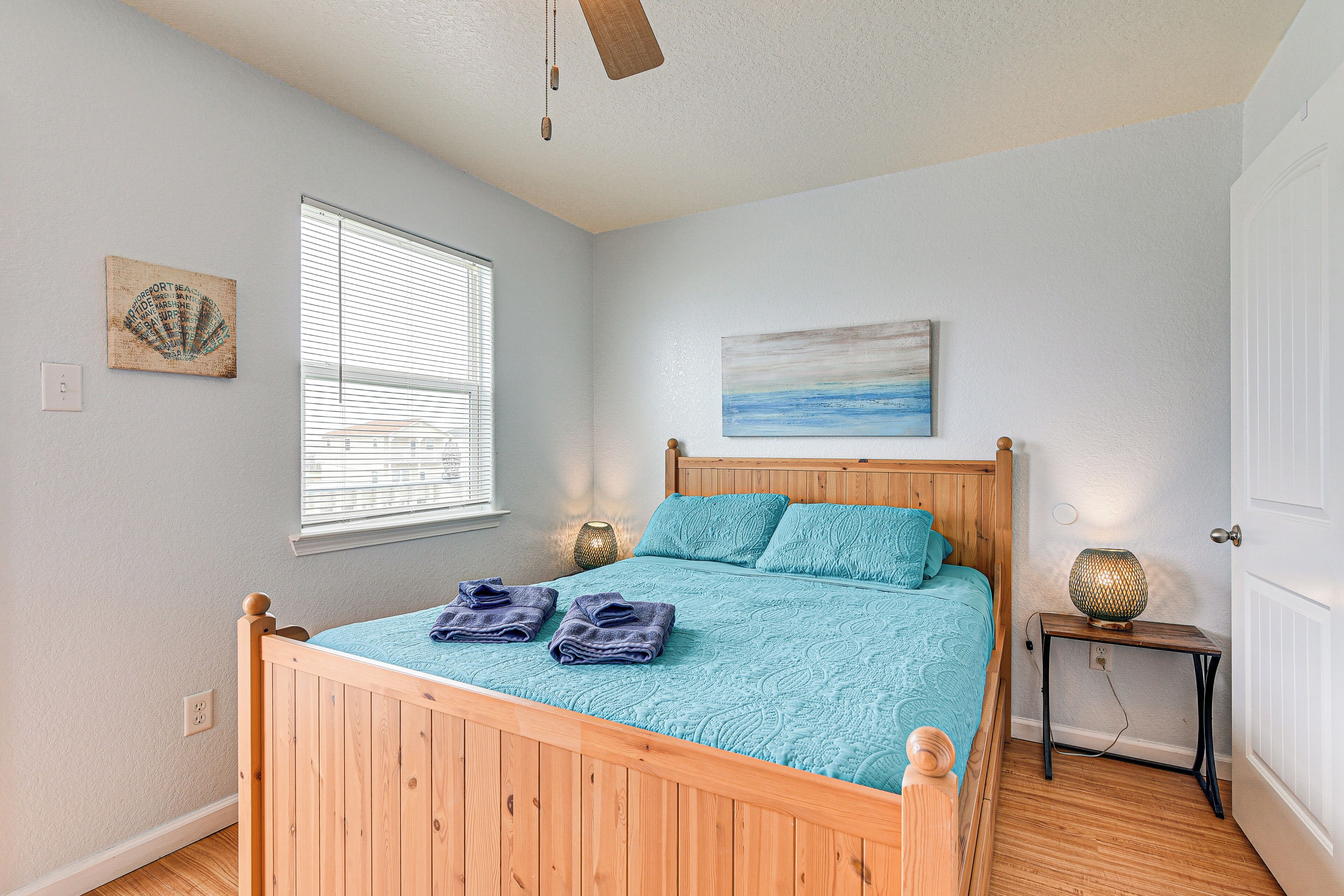 A bedroom with a wooden bed, a window with blinds, a wall-mounted painting, and a bedside table with a lamp.