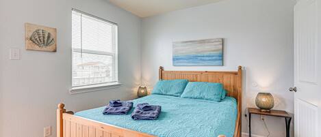 A bedroom with a wooden bed, a window with blinds, a wall-mounted painting, and a bedside table with a lamp.