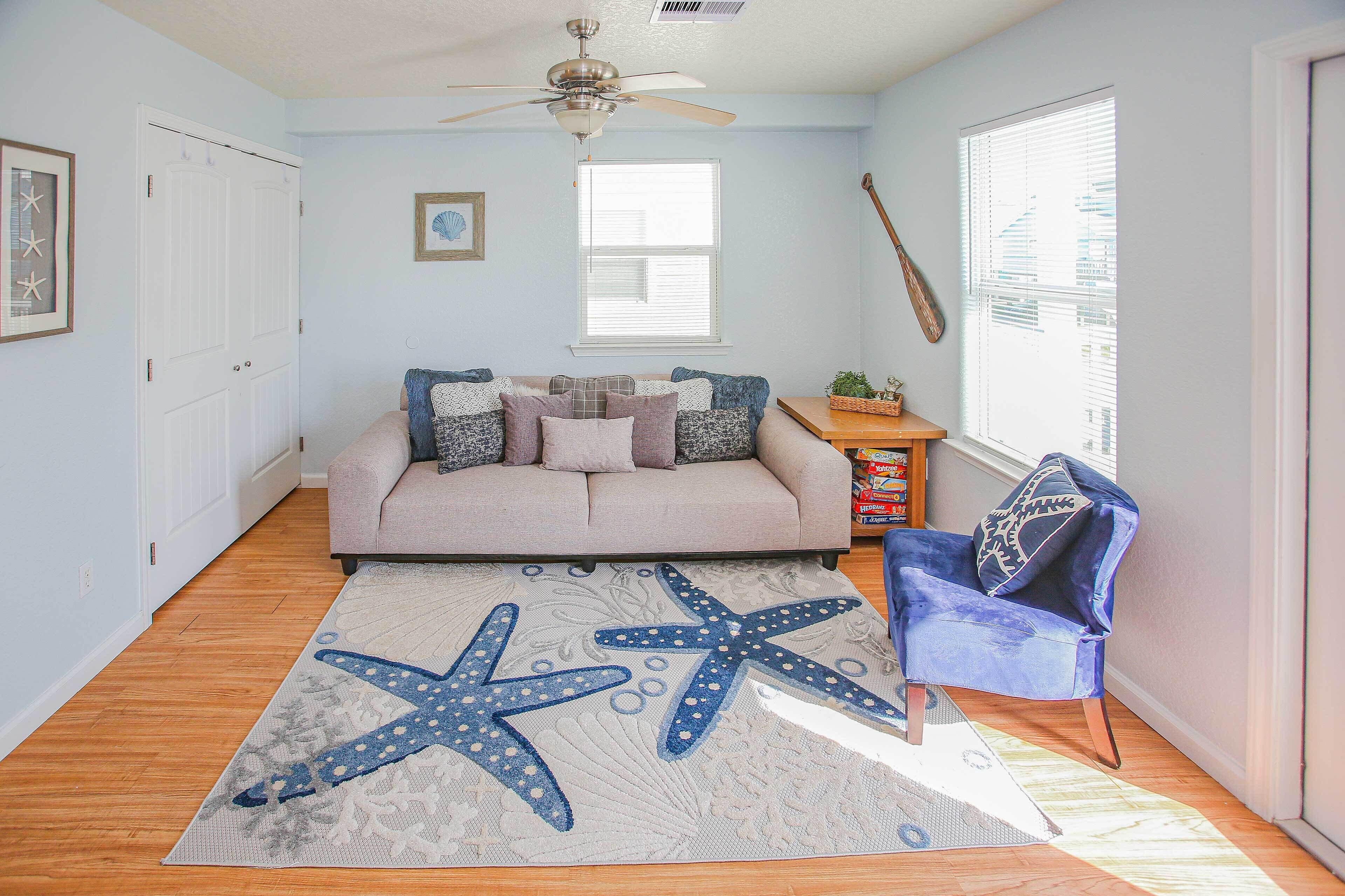 A living room with a beige sofa, starfish rug, wooden flooring, and a ceiling fan.