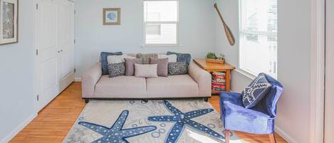 A living room with a beige sofa, starfish rug, wooden flooring, and a ceiling fan.
