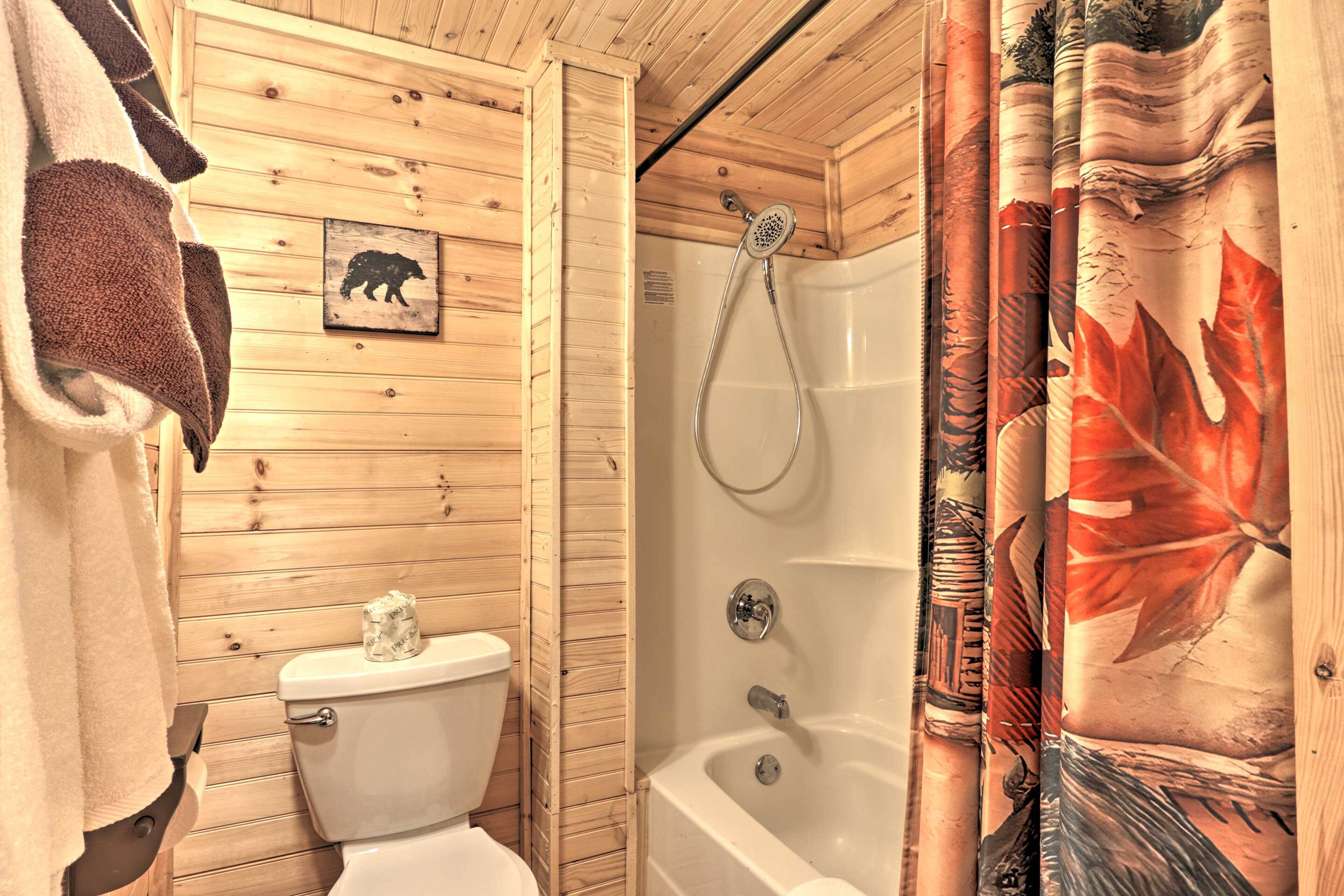 A wooden cabin bathroom with a toilet, shower, and a bear-themed wall decal.