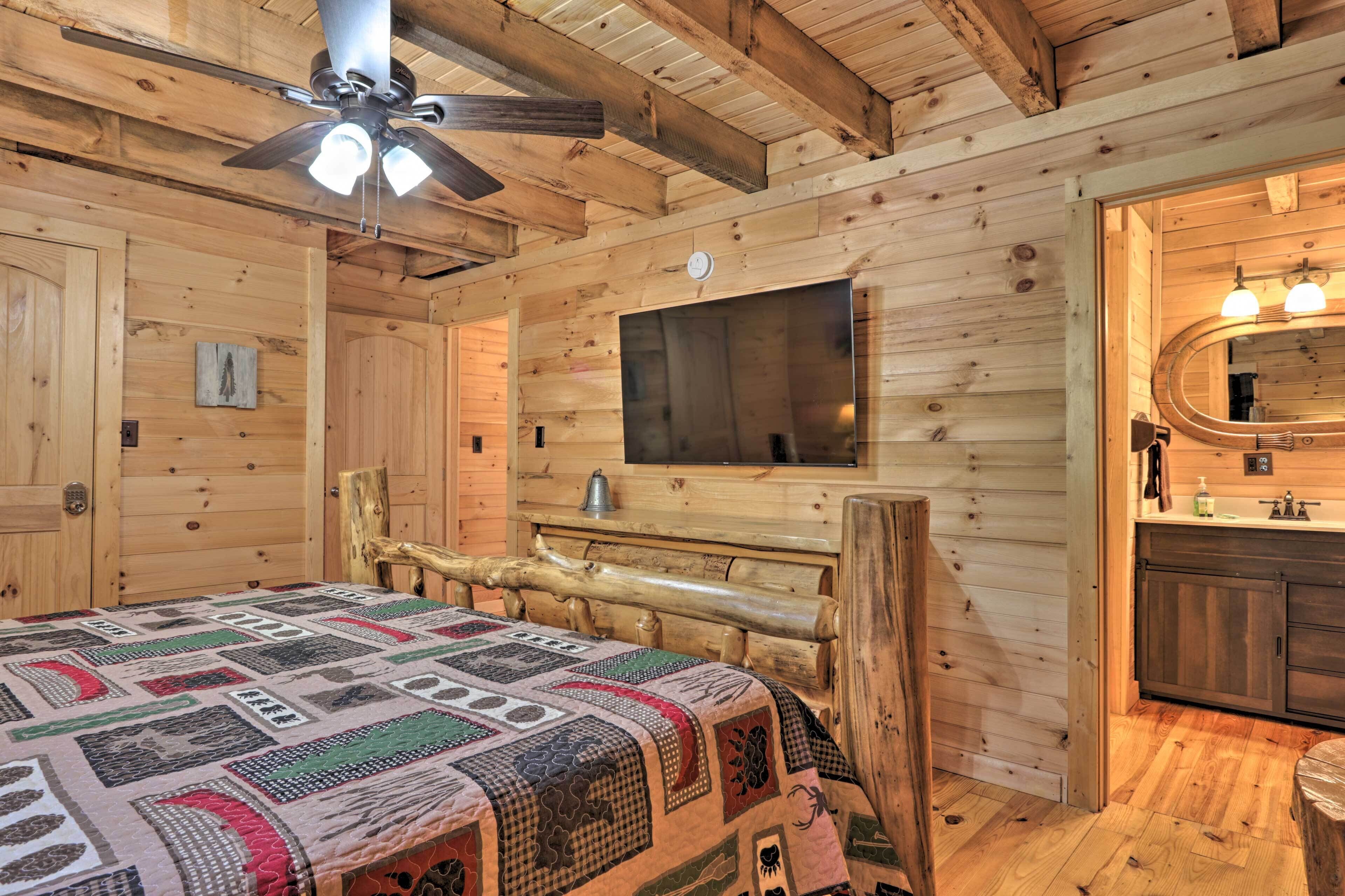 L’intérieur d’un chalet en bois comprend un lit, un banc en bois, un téléviseur et une salle de bain avec un miroir et un lavabo.