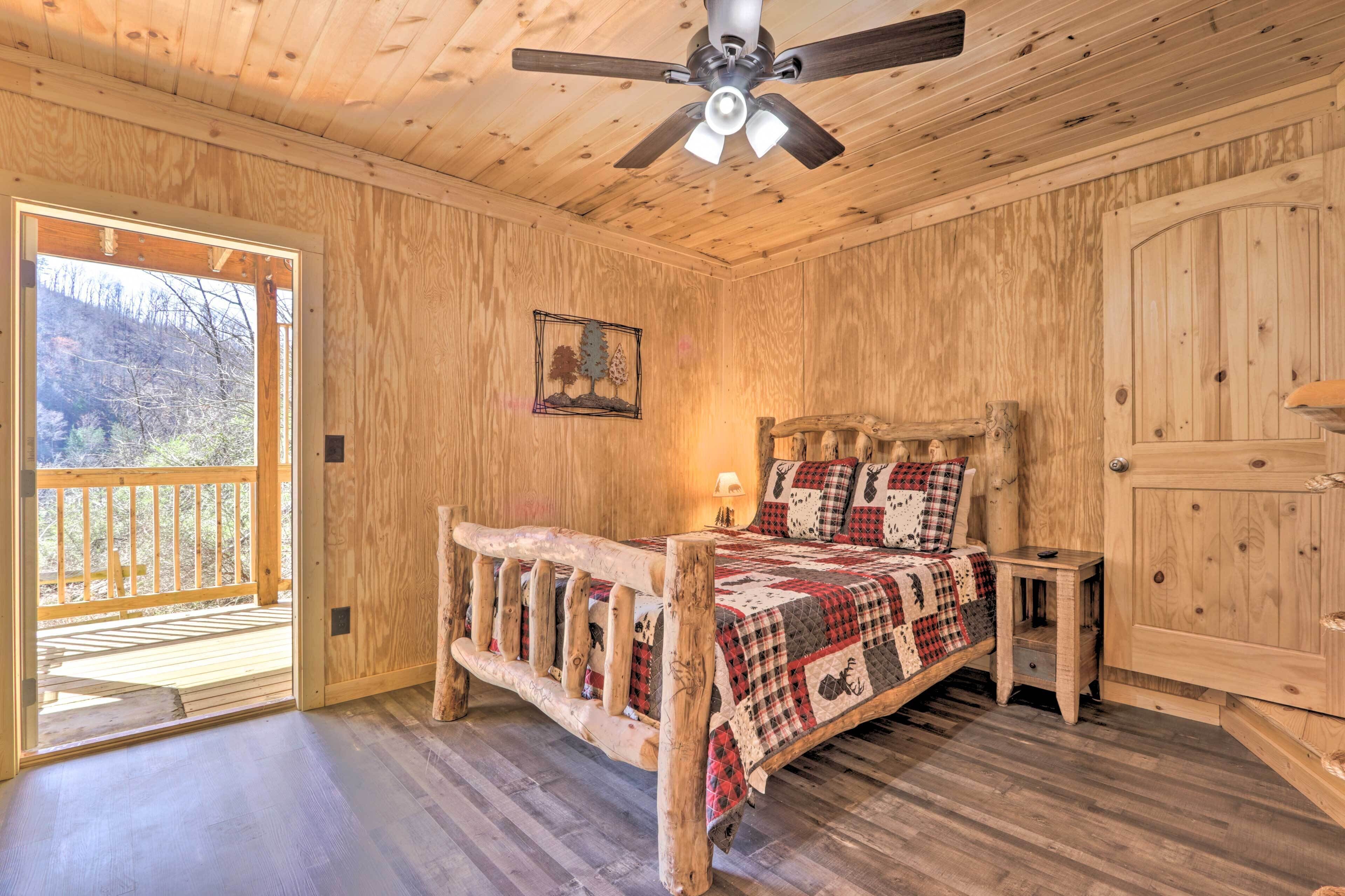 A wooden room with a bed, a ceiling fan, a door, and a window.