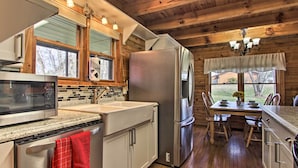 A modern kitchen with stainless steel appliances, wooden cabinets, and a dining area with a table and chairs. - Rustic Cabin w/ Screened Deck: 8 Mi to Dollywood (Sevierville)