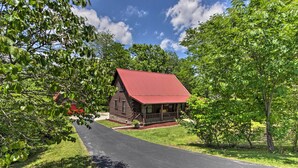 A wooden cabin with a red roof, surrounded by lush greenery and a paved driveway. - Rustic Cabin w/ Screened Deck: 8 Mi to Dollywood (Sevierville)