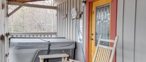 A covered porch with a hot tub, a wooden chair, and a door with a red frame.