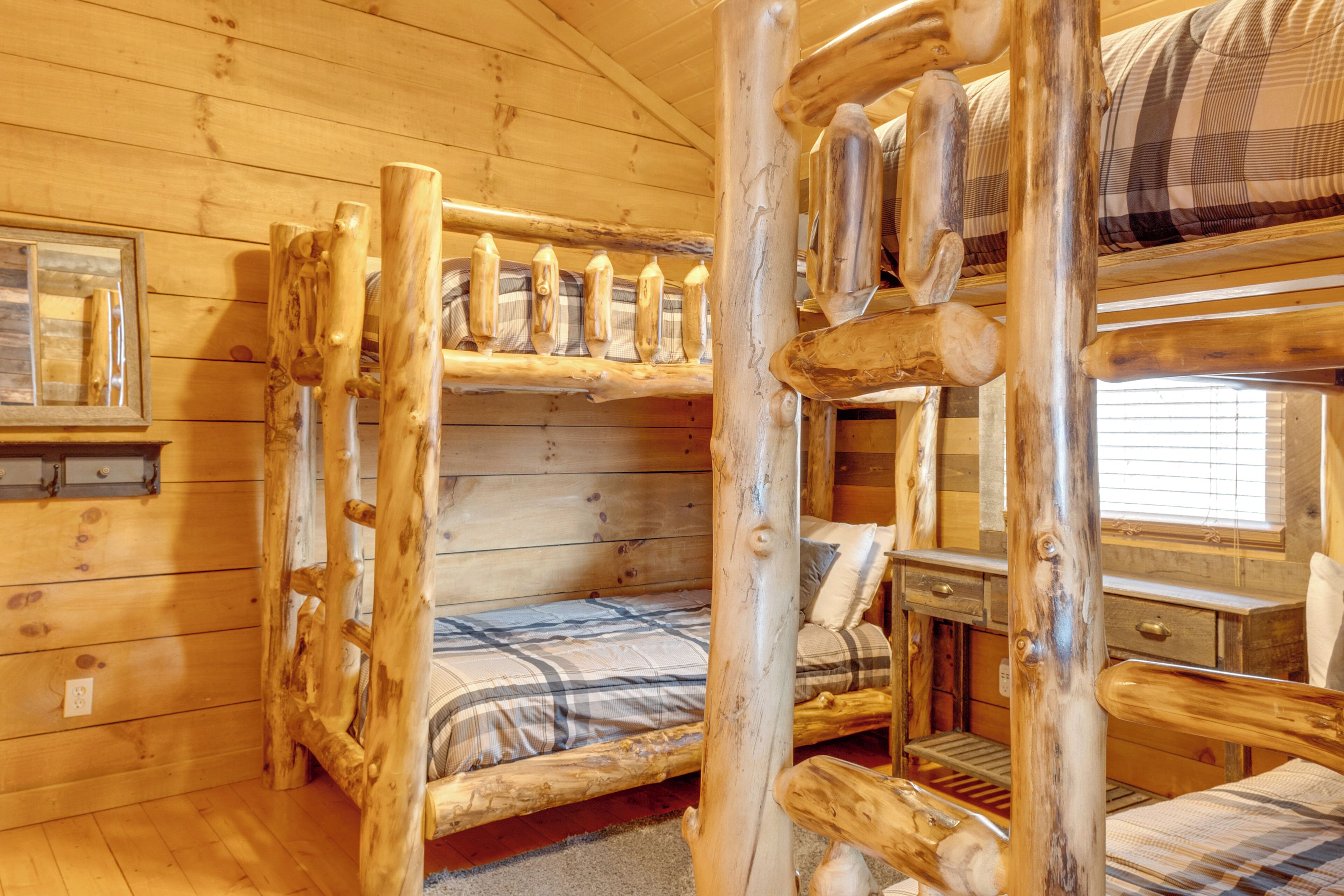 Une cabine avec un lit superposé et un lit simple, des murs en bois et une fenêtre avec des stores.