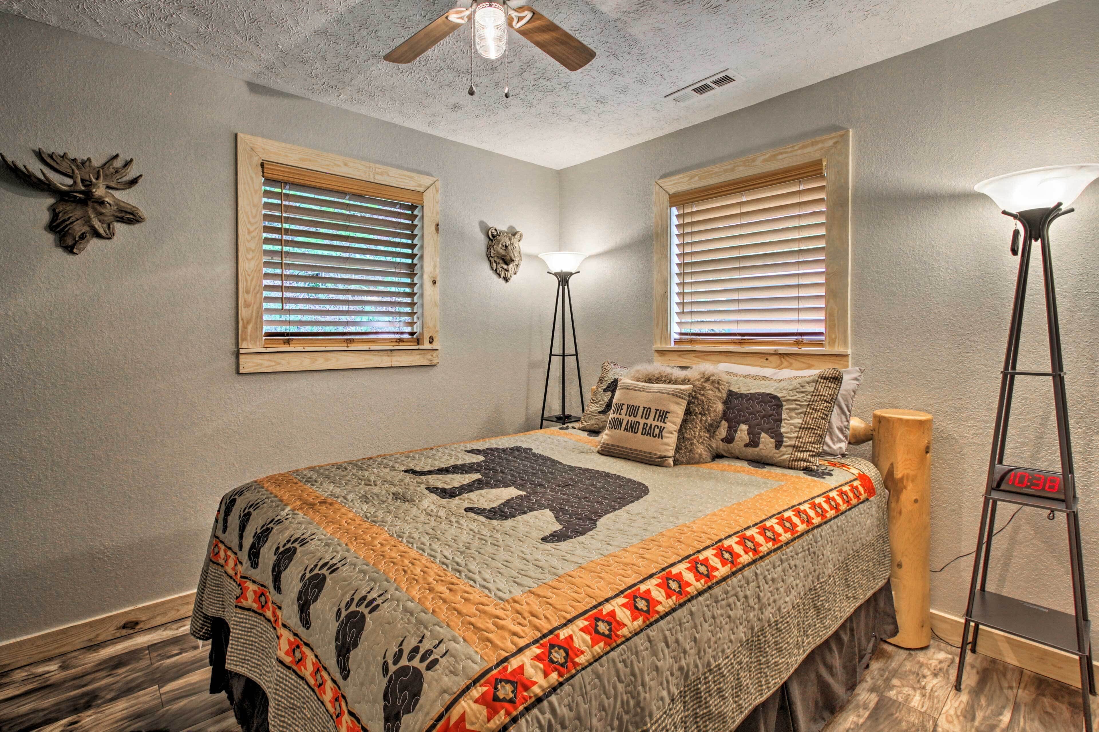 A bedroom with a bed, two windows with blinds, a ceiling fan, a floor lamp, and wall decorations.