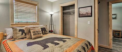 A bedroom with a large bed, a window with blinds, a floor lamp, a coat rack, and a door leading to another room.