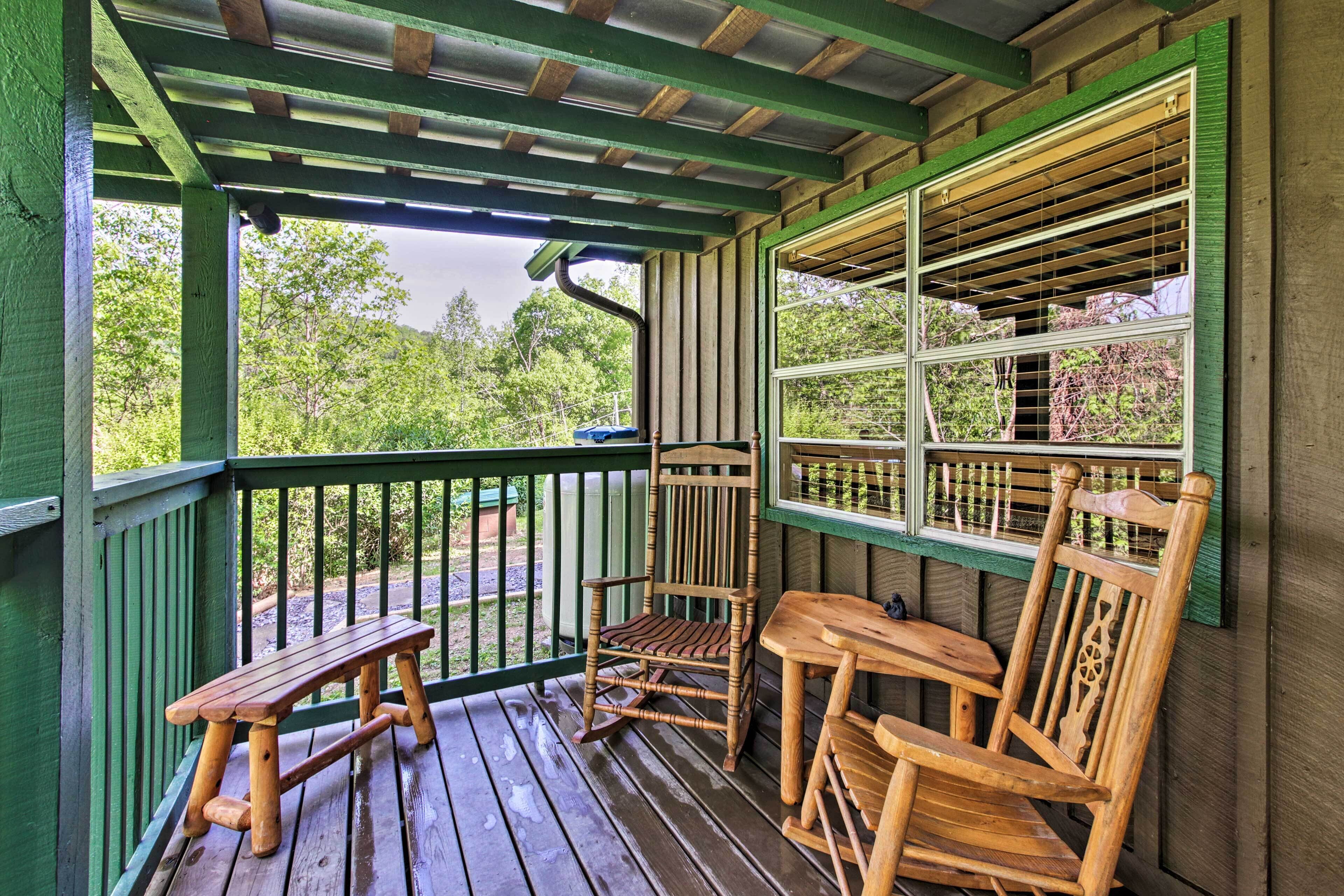 A wooden porch with a bench and two rocking chairs, a table, and a window with blinds.