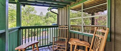 A wooden porch with a bench and two rocking chairs, a table, and a window with blinds.
